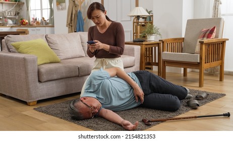 Asian Female Adult Granddaughter Trying To Awake His Unconscious Grandfather While Making Emergency Call On Phone After Fall Accident At Home