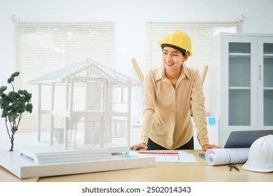 An Asian female architect analyzes blueprints at her desk in the office. She specializes in house design, focusing on roofs and walls, and collaborates with construction contractors in her company. - Powered by Shutterstock