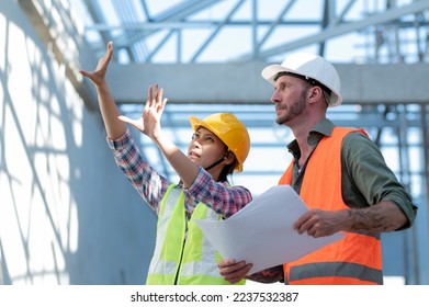 Asian female architect explaining design to white male engineer for building decoration, young building owner listens to report on construction results, side shot. - Powered by Shutterstock