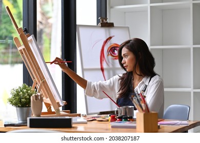 Asian female Artist painting picture  on canvas at creative workplace.