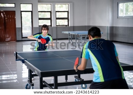 Asian female athlete preparing to serve against male athlete at ping pong table