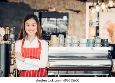 Asian female barista wear red apron crossed her arms at counter bar in front of coffee making machine with smile face,cafe service concept,owner business start up - Powered by Shutterstock