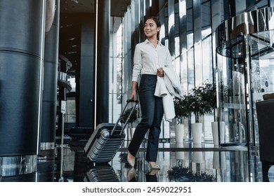 Asian female business traveler walking in airport hallway. Elegant young woman walking and pulling her suitcase in the airport terminal. Business travel concept - Powered by Shutterstock