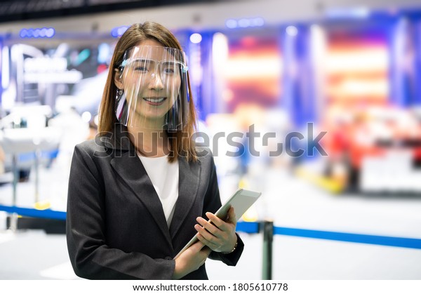 Asian female car seller\
wearing face mask presents detail of vehicle while conoravirus\
pandemic