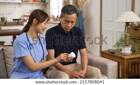 asian female caregiver explaining prescription to senior man patient on the sofa during home visit. she holds a drug bottle and talking with hand gestures