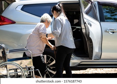 Asian Female Caregiver Helping Disabled Elderly Woman In Wheelchair To Get Into The Car,helpful Daughter Care And Support Senior Mother To Stand Up From Wheelchair In Outdoor, Caring For Old People