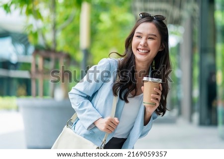 Asian female casual relax digital nomad freelance expat programer smart casual cloth walking on sidewalk urban city with holding coffee cup smiling cheerful positive feeling downshifting lifestyle