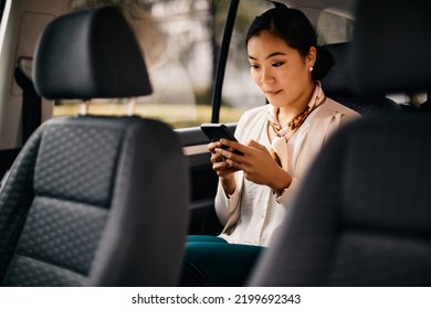 Asian Female CEO Texting On Mobile Phone While Commuting To Work In A Car.