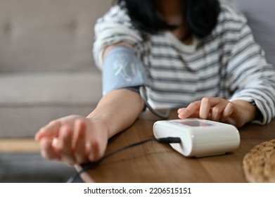 An Asian Female Checking Her Blood Pressure And Heart Rate With Blood Pressure Monitor Machine By Herself At Home. Health Care And Medical Concept. Cropped Shot