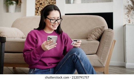 Asian Female Client Holding Banking Credit Card And Smart Phone Involved In Verification Process In Mobile Application. Happy Woman Doing Payments Online Or Shopping In Internet Store