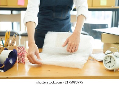Asian female clothes shop owner folding a t-shirt and packing in a cardboard parcel box. Asian businesswoman startup entrepreneur SME owner picking up a yellow shirt before packing it in an inner box.