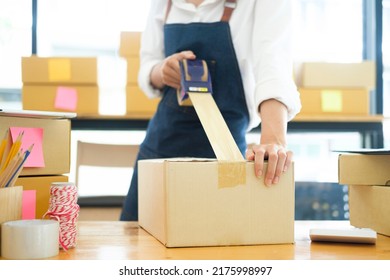Asian female clothes shop owner folding a t-shirt and packing in a cardboard parcel box. Asian businesswoman startup entrepreneur SME owner picking up a yellow shirt before packing it in an inner box.