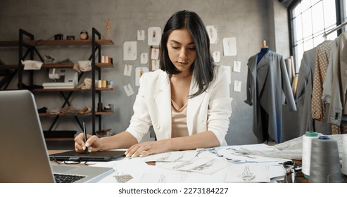 Asian female clothing designer is drawing her sketches on graphics tablet, preparing her new collection - fashion, success concept  - Powered by Shutterstock