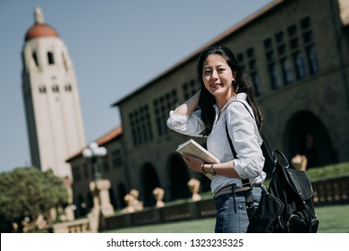 Asian Female College Student Study Abroad Carrying Backpack And School Book Standing Outdoor University On Sunny Day America. Young Woman Exchange Learn Language English Speaking Countries