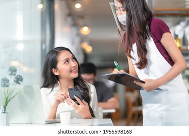 Asian female customer order food drink from smartphone digital menu social contactless to waitress staff ,Smiling millennial waitress with paper chart taking order from young asian female customer