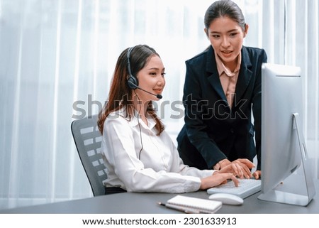 Asian female customer support operator wearing headset is guided by her supportive manager. Experienced colleague help operator handle a call with a client, providing advice and guidance. Enthusiastic