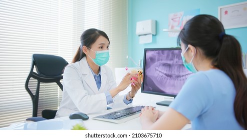 asian female dentist showing teeth xray at dental clinic - she teaches patient for teeth brushing and tooth decay by denture model while they wear protective face mask to prevent COVID19