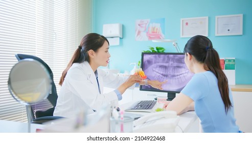 Asian Female Dentist Showing Teeth Xray At Dental Clinic - She Introduces Patient For Dental Implant By Denture Model