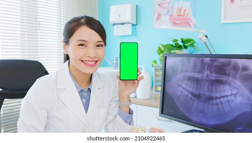 Asian Female Dentist Shows Teeth Xray On Computer Monitor In Hospital - She Holds Green Screen Mobile Phone