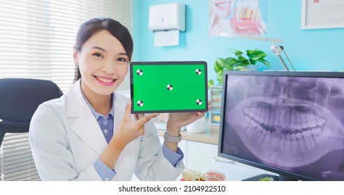 Asian Female Dentist Shows Teeth Xray On Computer Monitor In Hospital - She Holds Green Screen Digital Tablet