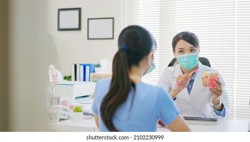 Asian Female Dentist Teaches Patient For Teeth Brushing And Tooth Decay By Denture Model While They Wear Protective Face Mask To Prevent COVID19