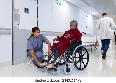 Asian female doctor checking leg of diverse senior female patient in wheelchair in hospital corridor. Hospital, medical and healthcare services. - Powered by Shutterstock