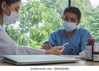 Asian Female Doctor Healthy Consulting, Blood Pressure Check-up Of A Male Patient With Face Mask In A Clinic. Processing With A Smartphone For Medication Treatment.