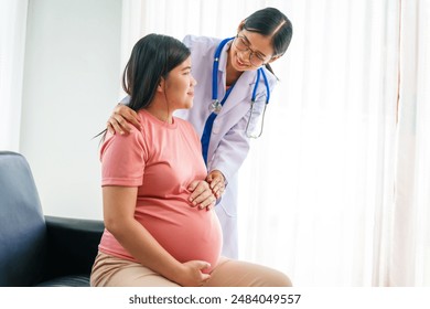 Asian female doctor nurse encouragement to a pregnant woman on a sofa, using ultrasound and stethoscope, addressing medical conditions like edema, varicose veins, and pregnancy-induced hypertension. - Powered by Shutterstock