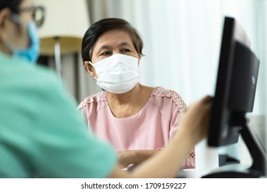 Asian Female Doctor Or Nurse In Green Uniform Talking Giving Advice To Elderly Woman Patient In Pink Cloth And Looking To Computer Screen Monitor Together In Hospital. Disease, Ill, Flu, Sick. 