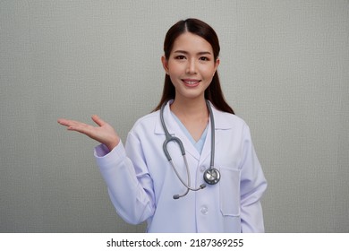 An Asian female doctor puts her hand to the side to make a presentation. with a smile, put the headphones on her shoulder wearing a white coat. - Powered by Shutterstock