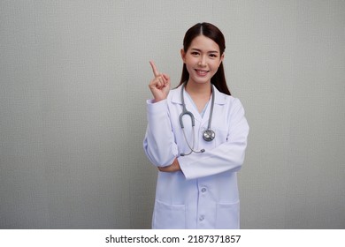 Asian female doctor standing with finger pointing at presentation with a bright smile and put the headphones on her shoulder wearing a white coat. - Powered by Shutterstock