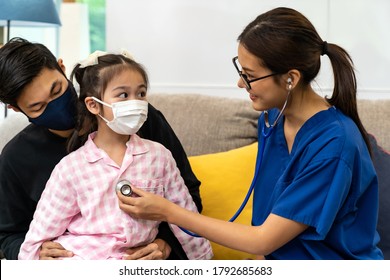 Asian Female Doctor Use Stethoscope To Listen Heartbeat Of Little Girl Child Sit With Her Father In Living Room While Doctor Visit At Home. Home Health Care Delivery And Doctor Visiting Concept.