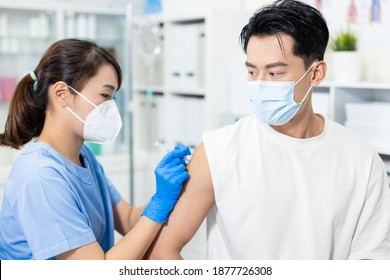 Asian Female Doctor Wearing Face Mask And Gloves Is Making A Vaccination In The Shoulder Of Male Patient In Hospital