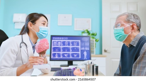 Asian Female Doctor Wearing Face Mask Is Showing A Model Of Brain And Explaining To Elder Senior Man Patient In Hospital