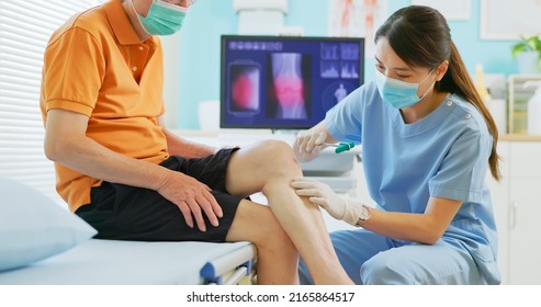 Asian Female Doctor Wearing Face Mask Is Examiniting Senior Elder Man Patient Joint With Percussion Hammer To Check His Knee Jerk Reflex