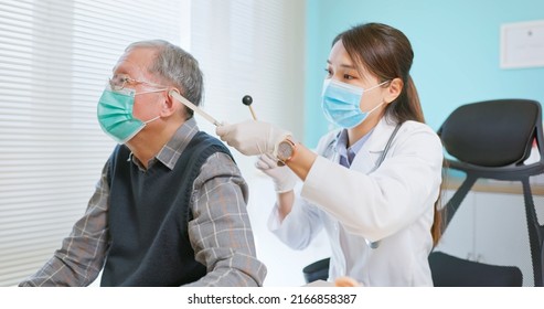 Asian Female Doctor Wearing Face Mask Is Using Tuning Fork For Hearing Tests To Elder Senior Man Patient In Hospital