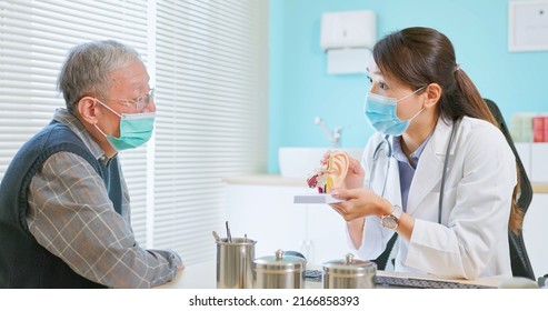 asian female doctor wearing face mask is showing ear canal model and explaining to elder senior man patient in hospital - Powered by Shutterstock