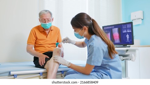 Asian Female Doctor Wearing Face Mask Is Examiniting Senior Elder Man Patient Joint With Percussion Hammer To Check His Knee Jerk Reflex