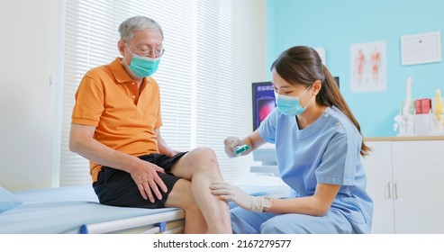 Asian Female Doctor Wearing Face Mask Is Examiniting Senior Elder Man Patient Joint With Percussion Hammer To Check His Knee Jerk Reflex