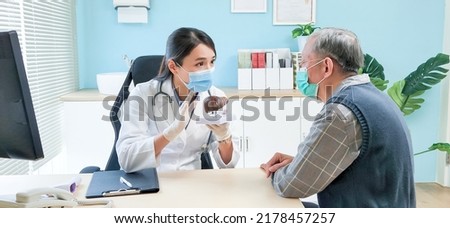 asian female doctor wearing face mask is showing liver model and explaining to elder senior man patient in hospital