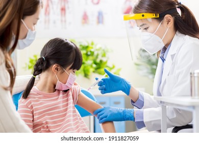 Asian Female Doctor Wearing Gloves And Isolation Mask Is Making A Vaccination In The Shoulder Of Child Patient With Her Mother At Hospital