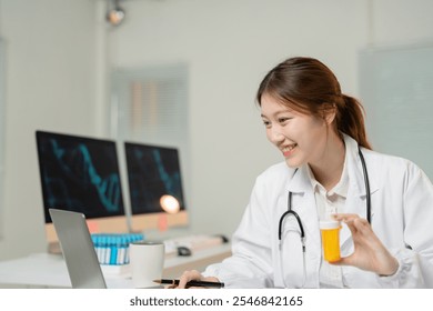 Asian female doctor wearing lab coat and stethoscope is holding a medicine bottle while having online consultation using laptop in her office - Powered by Shutterstock