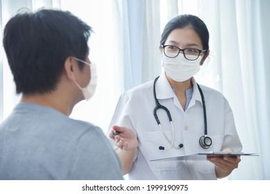 Asian Female Doctor Wearing Protective Face Mask Talking With Male Patient In Medical Room At Hospital.