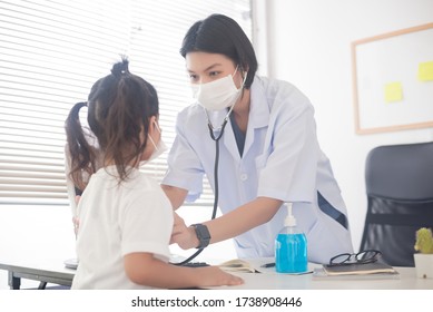 An Asian Female Doctor Wearing A Surgical Mask Is Checking The Child Patient's Heart Rate With A Stethoscope.