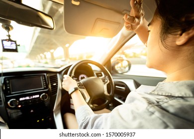 Asian female driver covering face by hand of bright sun,disturbed dazzled by sun light,difficulty in driving,young woman driving car feeling hot uncomfortable,risk of eye damage from ultraviole,UV ray