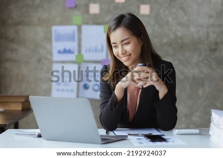 An Asian female employee sits with a coffee cup in the startup's marketing department office, she is a marketing, customer liaison and consulting worker. Marketing concept.