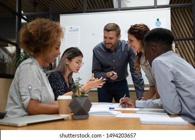 Asian female employee tell project idea talk to happy multiethnic team work group brainstorming discussing planning corporate strategy doing paperwork analyzing financial data at office meeting table