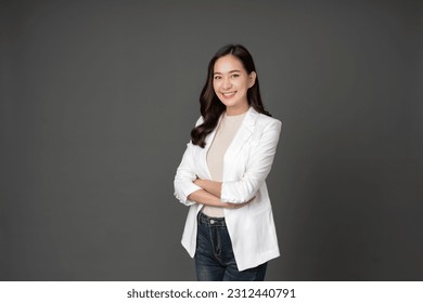 Asian female executive with long hair She smiled brightly and confidently stood with her arms crossed. She wore a white suit. and stand to take pictures with a gray scene in the studio