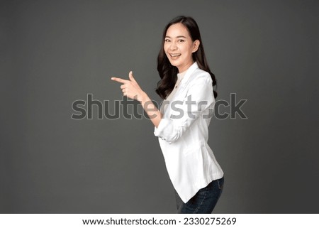 Asian female executive with long hair Turn sideways, point your finger towards the destination. Wearing a white suit and jeans, excited faces, bright smiles. Take a photo in the gray background studio