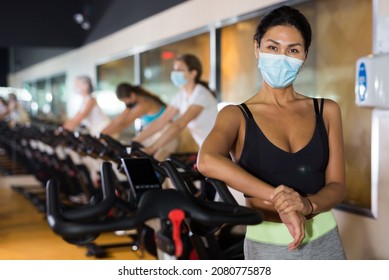 Asian Female In Face Mask With Fitness Bike During Cycling Class In Modern Gym